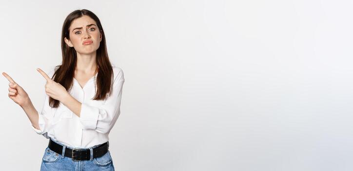 triste y decepcionado linda mujer, melancólico niña señalando dedos a logo, quejumbroso, malhumorado decepcionado, en pie en blusa terminado blanco antecedentes foto