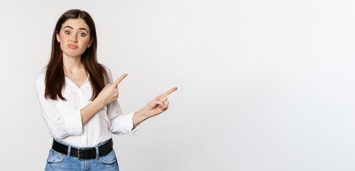 triste y decepcionado linda mujer, melancólico niña señalando dedos a logo, quejumbroso, malhumorado decepcionado, en pie en blusa terminado blanco antecedentes foto