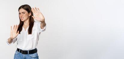 Displeased woman showing stop, rejection gesture, waving hands to decline, refuse of something ugly, standing over white background photo