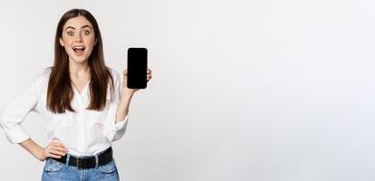 Happy smiling woman showing smartphone app interface, mobile phone screen, demonstrating promo offer, standing over white background photo