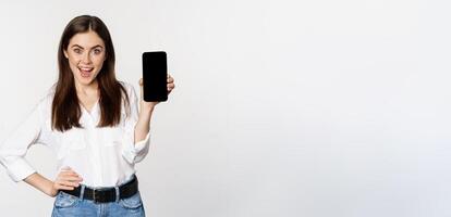 Happy smiling woman showing smartphone app interface, mobile phone screen, demonstrating promo offer, standing over white background photo