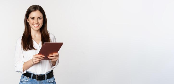 retrato de sonriente corporativo mujer mirando a digital tableta, laboral, en pie terminado blanco antecedentes foto