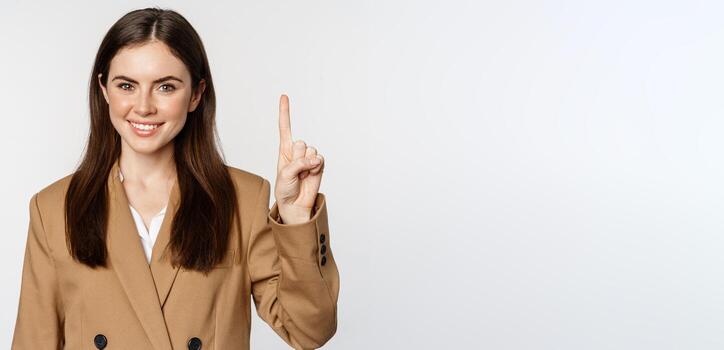 retrato de corporativo mujer, vendedora demostración número uno dedo y sonriente, en pie en traje terminado blanco antecedentes foto