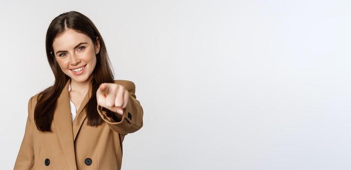 retrato de sonriente entusiasta mujer de negocios, vendedora señalando dedo a cámara y eligiendo, atractivo tú, en pie terminado blanco antecedentes foto