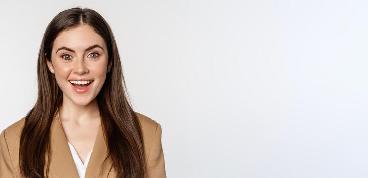 cerca arriba retrato de entusiasta corporativo mujer, mirando asombrado y emocionado a cámara, en pie en traje terminado blanco antecedentes foto