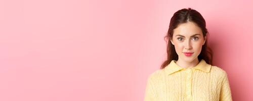 Close up of young glamour girl with cute make up, looking determined at camera, smiling, standing against pink background photo