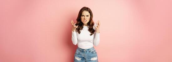 Annoyed and angry stylish girlfriend shaking hands outraged, arguing and complaining, standing furious against pink background photo