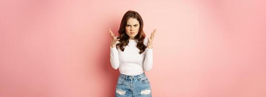 Annoyed and angry stylish girlfriend shaking hands outraged, arguing and complaining, standing furious against pink background photo