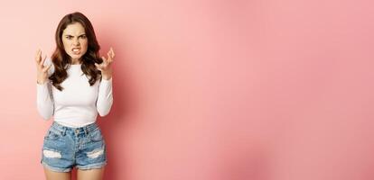 Annoyed and angry stylish girlfriend shaking hands outraged, arguing and complaining, standing furious against pink background photo
