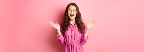Cheerful attractive lady scream of joy and clap hands, looking at camera, hear great news, rejoicing, standing over pink background photo
