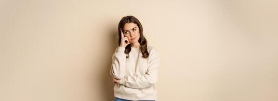 Annoyed woman, roll eyes and looking unamused, bothered and bored, standing over beige background photo