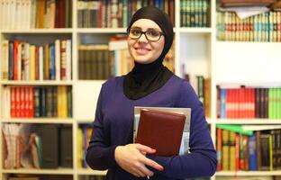 Smiling Islamic student with books in library photo