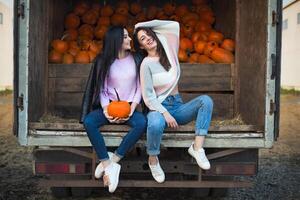 Fashionable beautiful young girlfriends together at the autumn pumpkin patch background. Having fun and posing photo