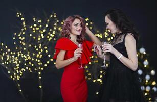 Smiling women in evening dresses with glasses of champagne over lights background photo