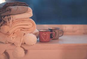Mugs and cozy plaids on window in night photo