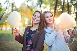 Fashionable beautiful young girlfriends with cotton candy together in the autumn park background. Having fun and posing. photo