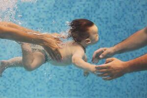 Father and mother teaching small child swimming underwater in the pool photo