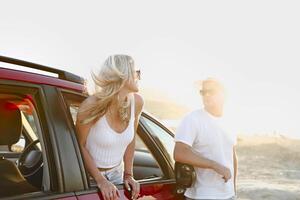 Young stylish couple in sunglasses hugging near red car by the sea photo