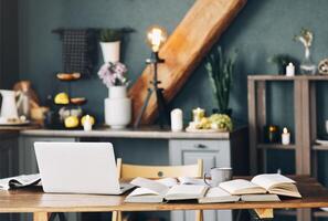 Open textbook with pen, laptop, stack of uncovered books and cup of coffee on table at home office photo