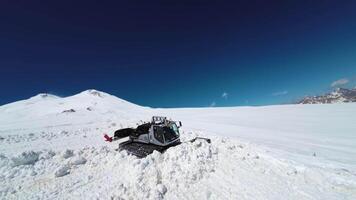 snowcat rides on a snowy parking lot at a winter ski resort in the mountains. Aerial top view from drone, clearing snow on winter slope of mountain resort video