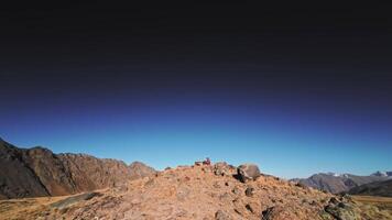 A white man wearing FPV goggles and a helmet sits in the mountains and controls an FPV acrodrone quadcopter flying around him. Dynamic footage of a drone pilot against the backdrop of epic mountains video