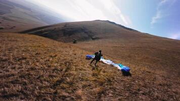 FPV aerial view of flying next to a paraglider after landing in a mountainous area. Filmed with a sports drone. The athlete collects his parachute after landing video