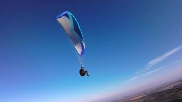 Aerial view from a sports FPV drone. A paraglider athlete flies near the slopes of a small mountain. Free paragliding flight over rural fields in autumn from FPV drone video