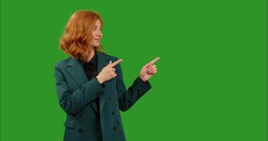 Woman smiling and looking at camera pointing her fingers at left top side over green screen background. video