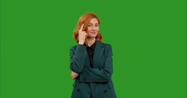 Confident woman on green screen background looking at camera and taps her temple as to think with her finger and points. video