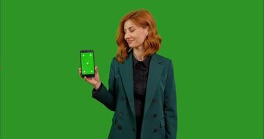 Portrait of business woman showing chroma key smartphone to camera with smile and ok sigh over green screen background. video