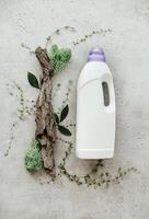Composition with bottle of laundry detergent by tree bark, tiny mosses and grass on light concrete background photo