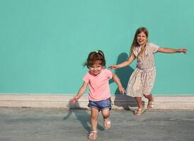 Cheerful little sisters in colorful dresses runing against green wall photo