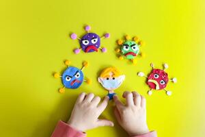Clay characters on yellow background with hands of the kid. Corona virus, covid-19. Care and save concept photo