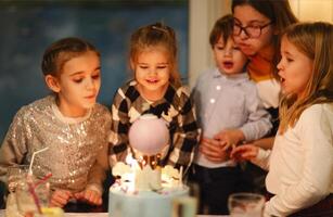 Group of joyful little kids celebrating birthday party and blowing candles on cake photo