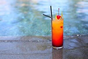 Glass with a bright tequila sunrise cocktail by the pool. photo