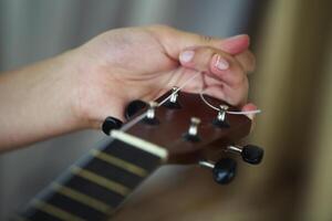 Tuning the string of ukulele, human hands, closeup photo