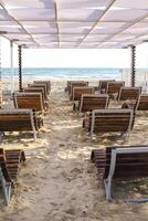 Beautiful view of summer seaside and sand beach with empty comfortable sunbeds under sunshade photo