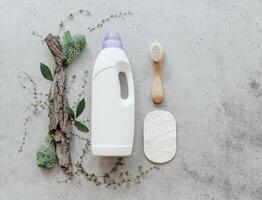 Composition with bottle of laundry detergent by tree bark, tiny mosses and grass on light concrete background photo