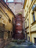 A view of an abandoned brick chimney in a dilapidated urban alley, surrounded by weathered walls and graffiti. The image captures the sense of decay and urban neglect, highlighting the textures and colors of the aged bricks and crumbling plaster photo