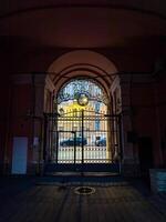 View through a gated archway showcasing intricate ironwork and a glimpse of a historic urban street bathed in evening light. Captured in a low-light setting, highlighting the contrast between the interior shadow and exterior illumination photo