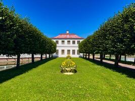 Elegant view of a manicured garden featuring symmetrical rows of trees and a historic building, surrounded by lush greenery and vibrant blue skies, highlighting the harmony of nature and architecture. photo