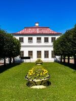 Elegant view of a manicured garden featuring symmetrical rows of trees and a historic building, surrounded by lush greenery and vibrant blue skies, highlighting the harmony of nature and architecture. photo