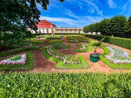 Vibrant view of a meticulously manicured garden featuring colorful flower beds and ornamental plants, surrounded by lush greenery and set against a bright blue sky, perfect for a peaceful stroll photo
