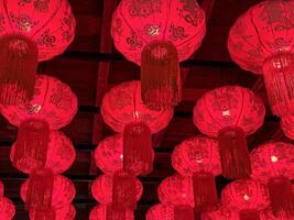 Close-up of traditional red Chinese lanterns with intricate patterns and tassels hanging from a ceiling, illuminated to create a warm festive ambiance, perfect for celebrating Chinese New Year or other cultural events photo