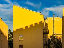 A striking image of bright yellow buildings in St. Petersburg, Russia, with shadows creating intriguing patterns on the walls. The vibrant yellow contrasts beautifully with the blue sky, creating a captivating and cheerful urban scene photo