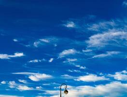 A captivating image of a clear blue sky adorned with delicate white clouds, highlighting a classic street lamp in the foreground. This serene scene evokes a sense of calm and tranquility, perfect for background or decorative purposes photo