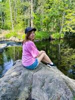 A girl enjoys a peaceful moment sitting by a serene forest river. Capturing the essence of tranquility and nature, this image is perfect for promoting outdoor adventures and relaxation photo