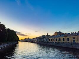A tranquil scene of a canal in St. Petersburg, Russia, captured at sunset. The calm water reflects the colorful sky, while historic buildings line the canal, creating a picturesque and peaceful evening view photo