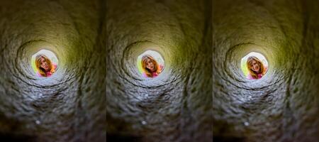 A young girl peers down a hole in granite, her face framed by the rugged stone. Her curious expression and the unique perspective create an engaging and playful scene, perfect for illustrating curiosity, exploration, and childhood adventures. photo
