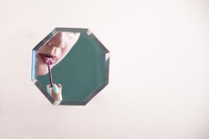 reflection of a woman in the mirror who paints her lips with lipstick, mirror hanging in zero gravity on peach fuzz background, photo